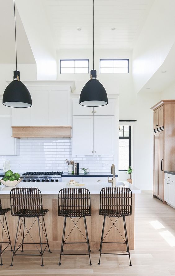 a modern kitchen with white shaker style cabinets, black countertops, a stained kitchen island and black metal stools