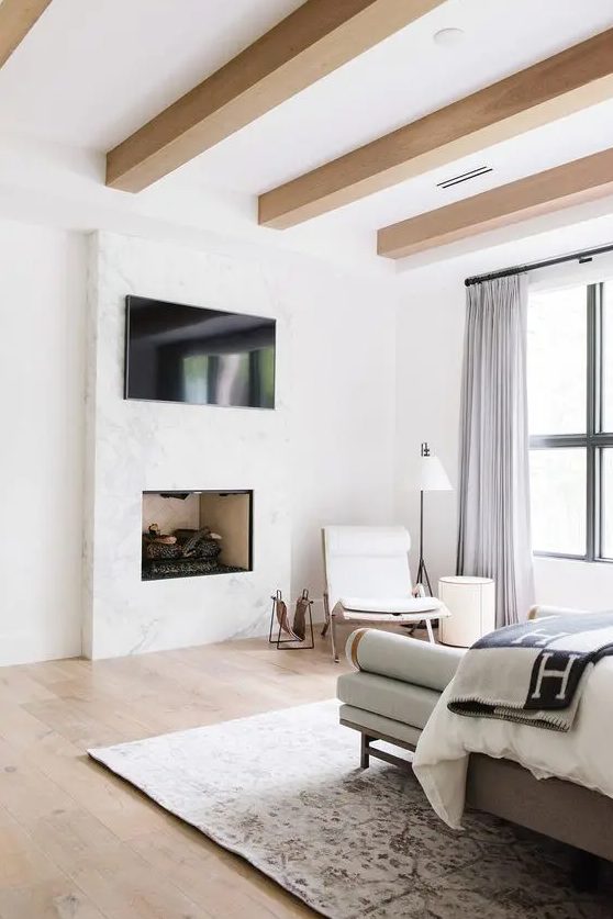 a modern neutral bedroom with sleek wooden beams, stylish furniture, a TV and a working fireplace built-in