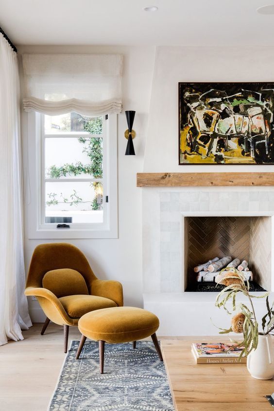 a modern nook with a brick clad fireplace, a wooden mantel, a mustard-colored chair with a footrest and a bold artwork for a chic look