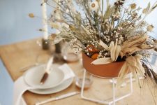 a modern organic Thanksgiving tablescape with white porcelain, greenery and a beautiful dried flower and herb centerpiece in a terracotta pot