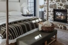 a modern rustic bedroom with a stone accent wall with a fireplace, a canopy bed, a leather bench, a large rug
