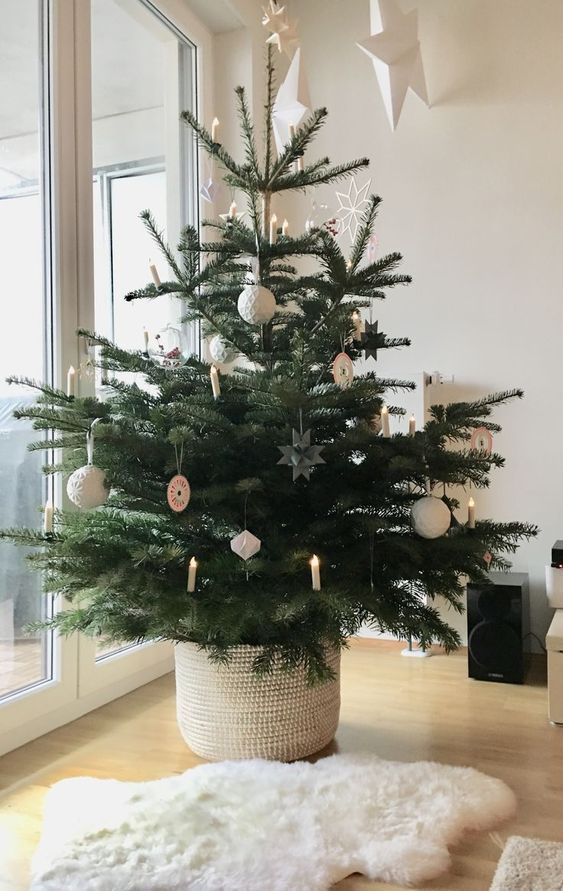 a modern to Scandi Christmas tree decorated with simple white and grey ornaments and lights as candles plus a white woven basket