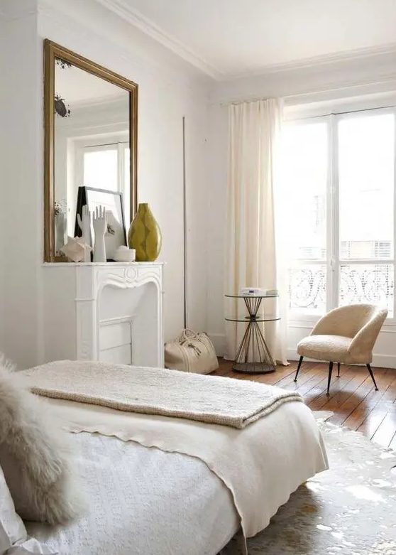 A neutral Parisian bedroom with a non working fireplace, neutral furniture and linens and pretty artworks