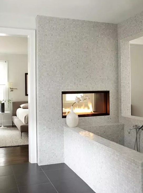 a neutral bathroom with small scale tiles, a double-sided fireplace, a bathtub clad with tiles is a chic idea to rock