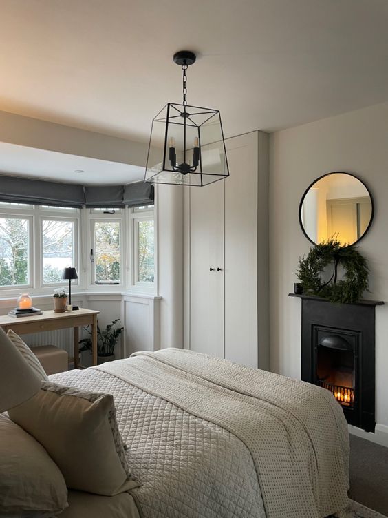 A neutral bedroom with a metal fireplace, a bed with neutral bedding, a built in wardrobe, a vanity at the window and some lamps