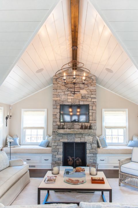 A neutral chic space with a stone clad fireplace, two built in benches with cushions and pillows plus a stone mantel