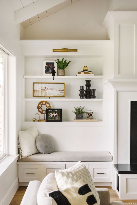 a neutral farmhouse nook with a chic built-in bench with pillows and built-in shelves over it next to the fireplace