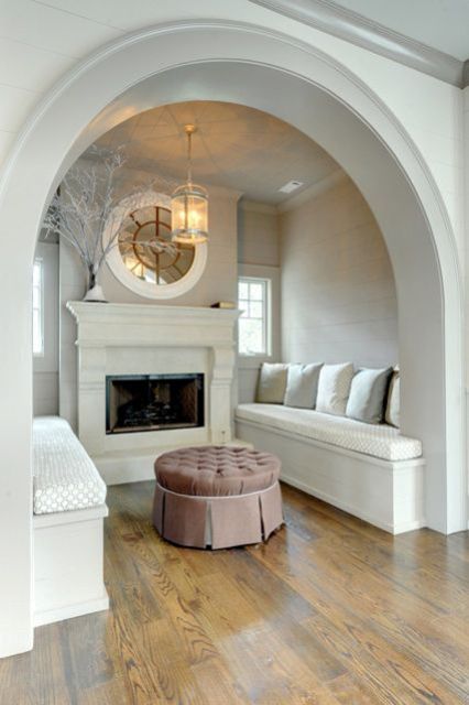 A neutral vintage conversation space with a built in fireplace, built in benches and pillows plus a round mirror and branches