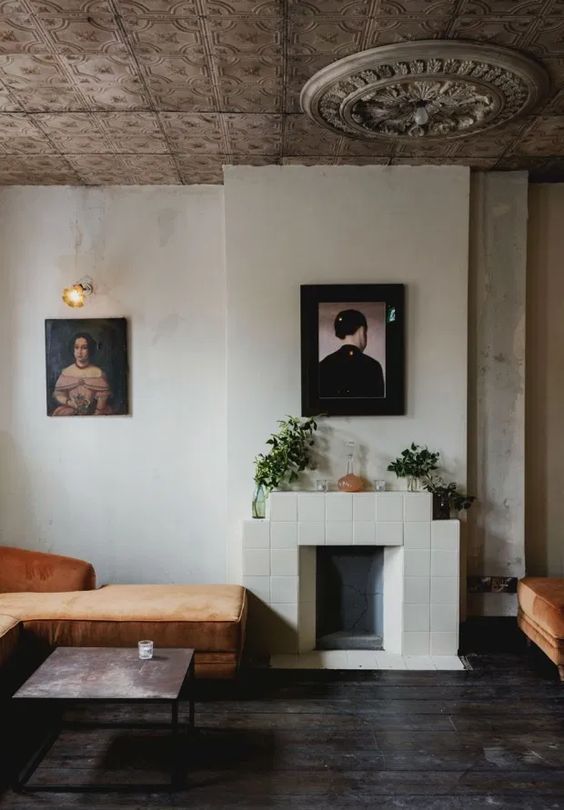 a quirky nook wiht a tiled fireplace, a rust-colored lounger, some artworks and potted plants is a lovely space