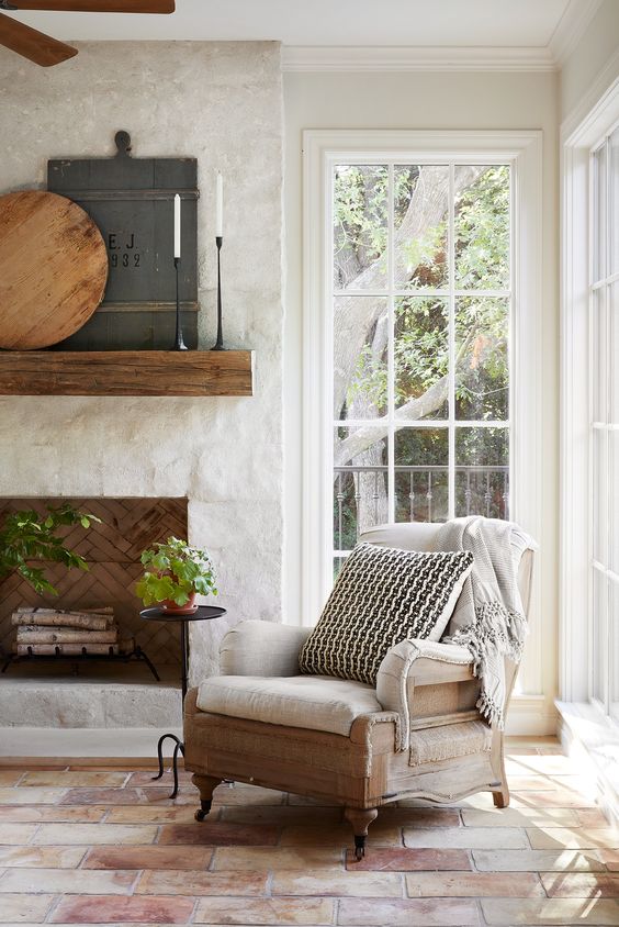 a refined farmhouse nook with a stone clad fireplace, a wooden mantel and a refined chair with a blanket and a pillow is cool