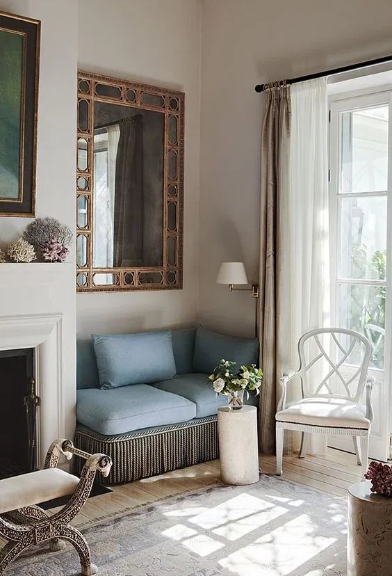 a refined nook with a white fireplace, a whimsy stool, a built-in blue sofa and a large mirror over it