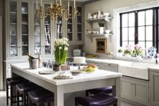 a refined vintage dove grey kitchen with shaker style cabinets, a vintage chandelier, a large kitchen island with purple stools