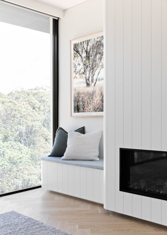 A serene nook with a wood clad built in fireplace, a built in bench with pillows and a lovely view plus a chic artwork