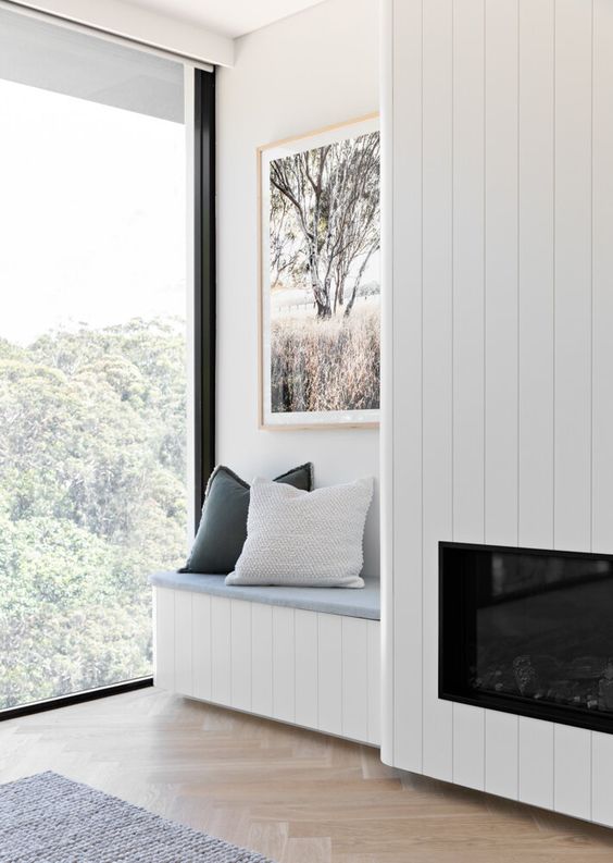 a serene nook with a wood clad built-in fireplace, a built-in bench with pillows and a lovely view plus a chic artwork