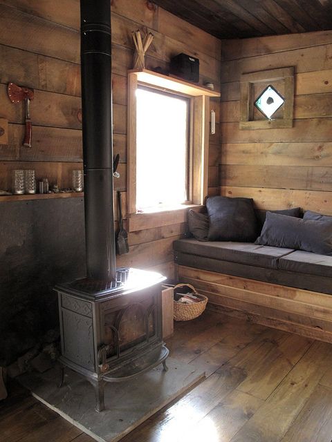 a simple cabin space with a vintage hearth and a wooden bench with cushions and pillows plus shelves and baskets is welcoming