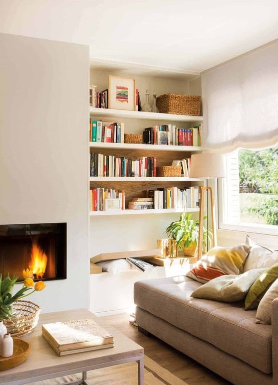 A sleek built in fireplace, a bench and built in shelves, a tan couhc with pillows form a cozy and welcoming reading nook