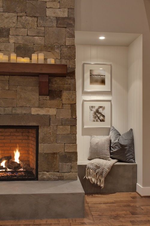 A stone clad fireplace with a concrete sill plate and a built in concrete seat with pillows for warming up