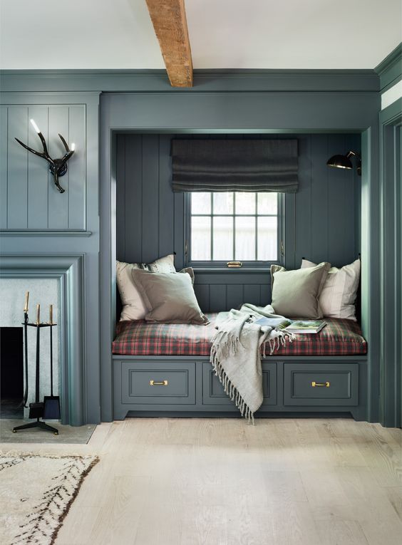 A stylish farmhouse space with a stone clad fireplace, a built in bench with drawers, a plaid cushion and neutral pillows