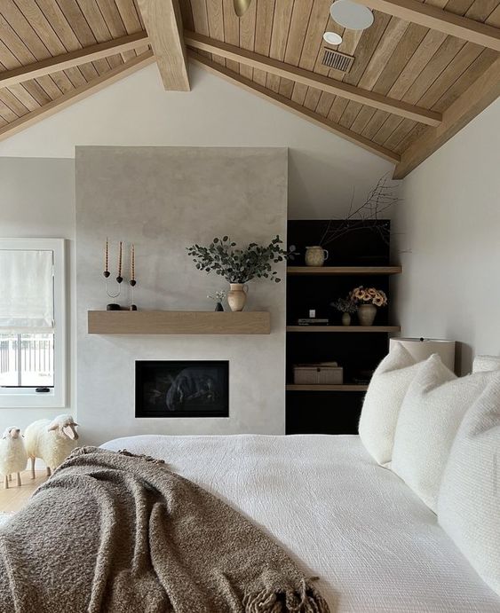 A stylish neutral bedroom with a built in fireplace, built in shelves, a bed with neutral bedding, sheep for decor