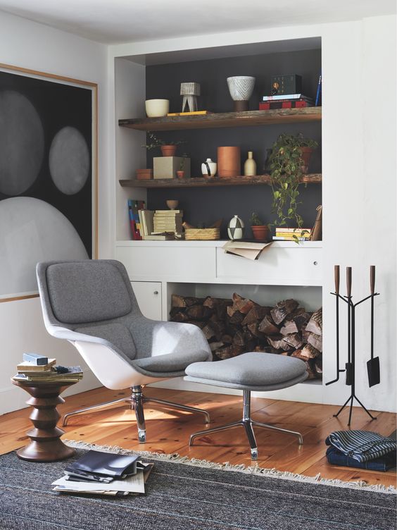 a stylish nook by the fire, with built-in shelves in a niche, a grey lounger with a footrest, some potted greenery