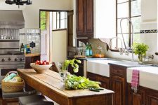 a vintage rustic kitchen with refined dark stained cabinets, a long table that doubles as a kitchen island and vintage chandeliers