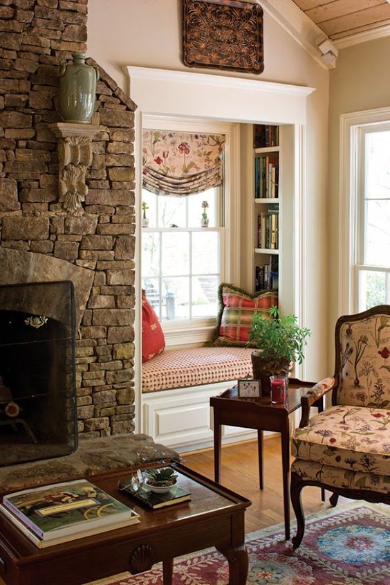 a vintage rustic space with a stone clad fireplace, a small built-in nook with built-in bookshelves and pillows and a floral chair with a table