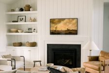a welcoming farmhouse living room with a built-in fireplace, a grey sofa, a leather chair, built-in shelves and a cabinet