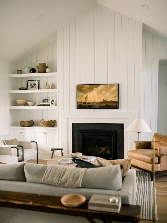 A welcoming farmhouse living room with a built in fireplace, a grey sofa, a leather chair, built in shelves and a cabinet