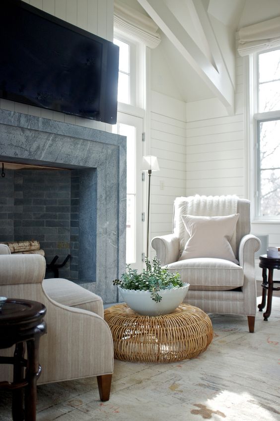 a welcoming farmhouse nook with a brick and stone clad fireplace, tan striped chairs, a rattan coffee table and a potted plant