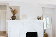 a white bedroom with a fireplace, a bed with white bedding, some decor and a floor mirror is an airy space