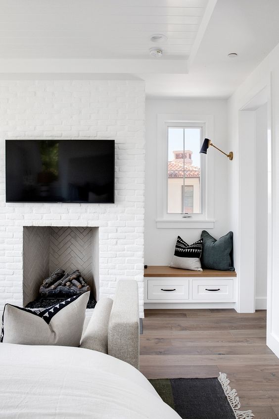 a white brick fireplace with firewood inside and a small built-in windowsill with drawers plus pillows is a welcoming nook