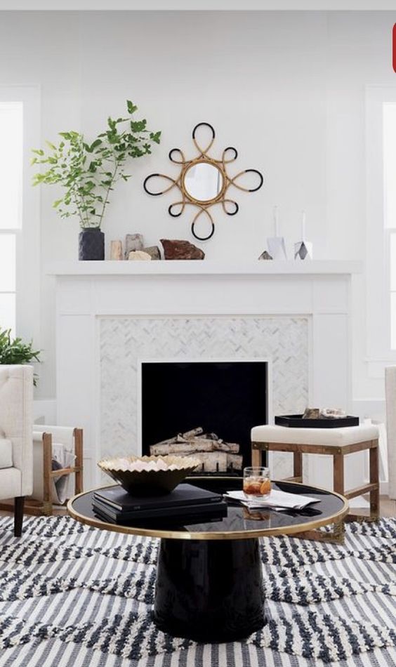 a white tile clad fireplace with firewood, a couple of stools, a mantel with greenery and rocks and a black round table