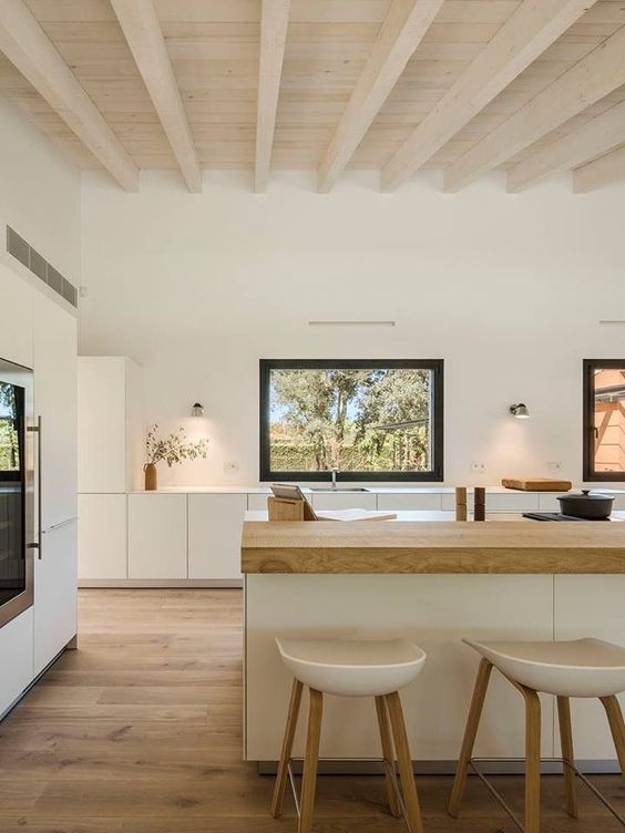an airy minimalist kitchen in white, with sleek cabinets, a large kitchen island with a butcherblock countertop and neutral stools