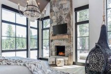 an ultra-modern chalet bedroom with a stone fireplace, a suspended chair, a catchy chandelier and lots of faux fur