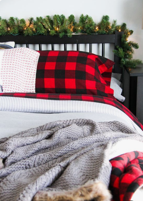 plaid and knit bedding, evergreens with lights bring astrong holiday feel to the bedroom