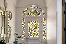 a catchy entryway with an arched door with stained glass and matching sidelights, a gallery wall of mirrors and a credenza
