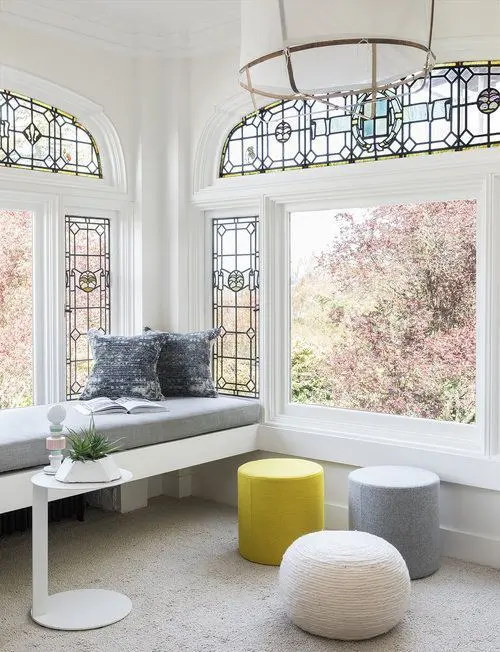 A chic space with vintage windows with stained glass but contemporary furniture   a built in bench, poufs and a table