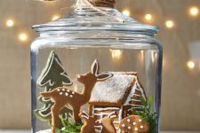 a lovely Christmas terrarium of a jar with faux snow, deer, hare, a small house and a Christmas tree plus greenery