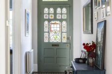 a pretty entryway with a green door with stained glass, a gallery wall, a black vanity with some art and pendant lamps