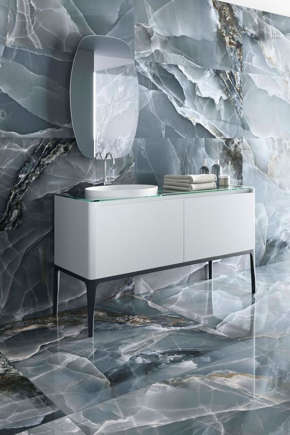 A sophisticated bathroom clad with grey onyx tiles looks jaw dropping, a white vanity and a catchy mirror add to the space