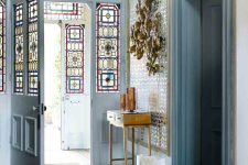 a stylish entryway with serenity blue doors and sidelights with stained glass, a heavy crystal chandelier and a stained console table