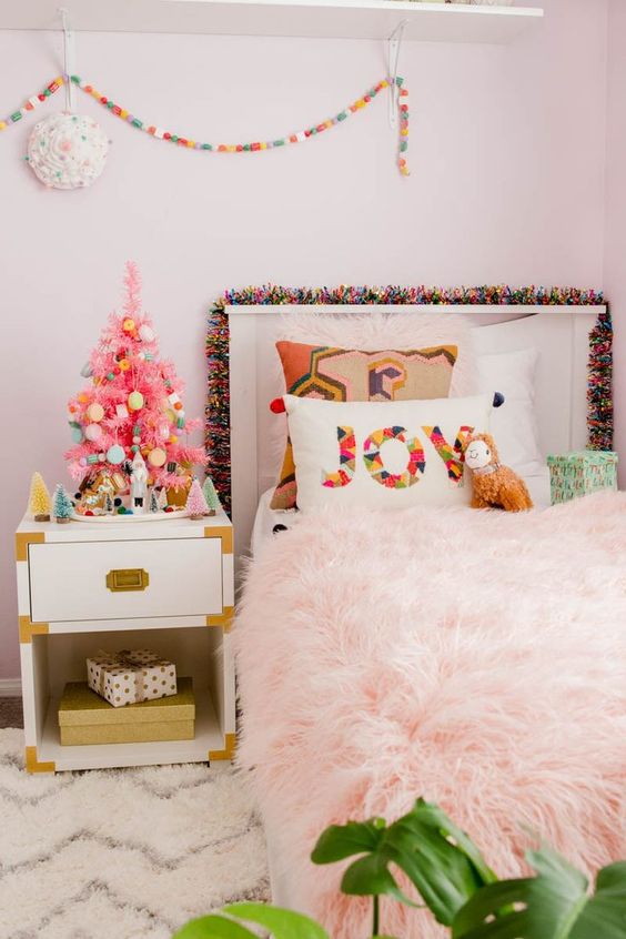 a tiny pink Christmas tree with colorful ornaments, a bright pompom garland and a printed pillow for holiday