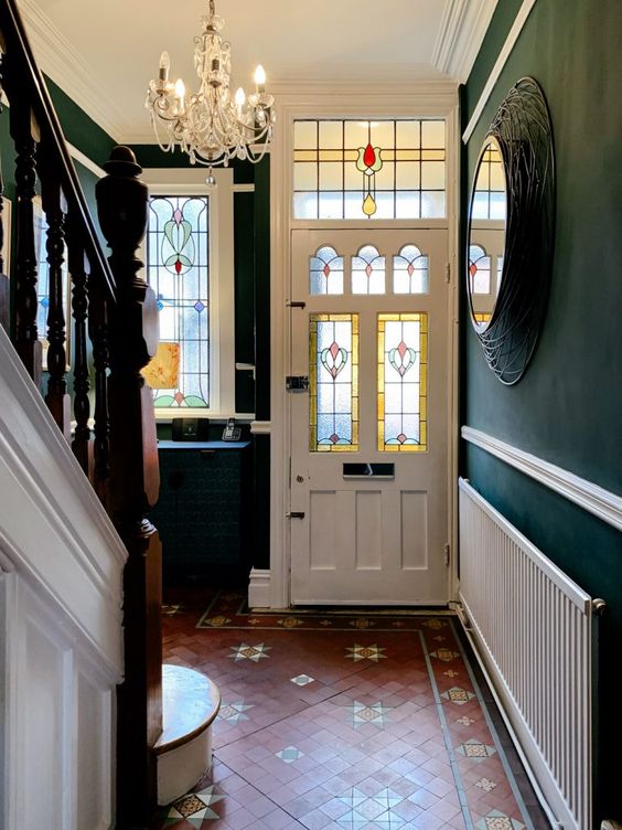 A vintage styled entryway with tiles on the floor, dark green walls, a crystal chandelier and a stained glass window and foor is wow
