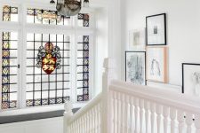 a white staircase, a windowsill bench and a window with stained glass, a crystal chandelier and a gallery wall