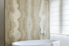 an organic bathroom in neutrals with an oval tub, a plywood stool and a beige onyx space divider that is a shower wall