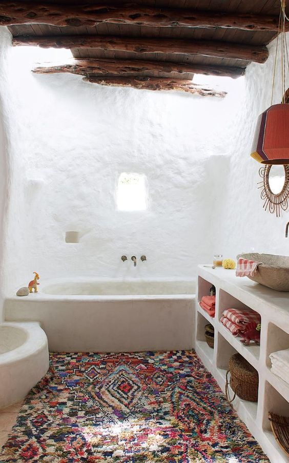 a boho bathroom with white walls, a stained ceiling with beams, a boho rug and a concrete vanity