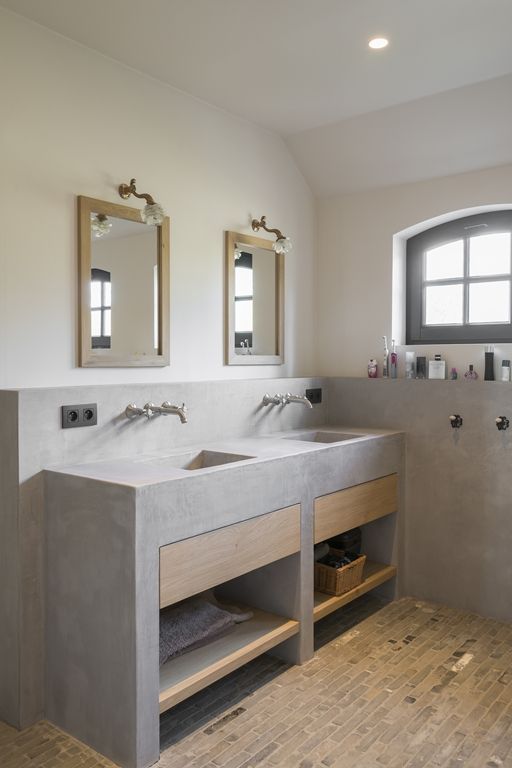 A catchy contemporary bathroom with a tiled floor, a built in concrete vanity with sinks, mirrors in wooden frames and wooden drawers