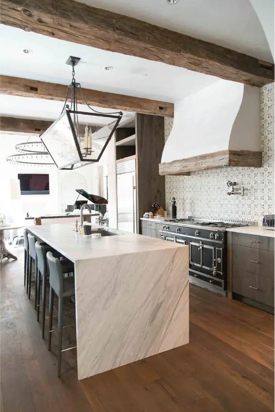 a catchy kitchen with dark cabinetry, a white stone kitchen island, rough wooden beams and a refined chandelier