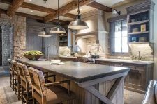 a chalet kitchen with rough wooden cabinetry and kitchen island, stone countertops, wooden beams and pendant lamps and vintage stools