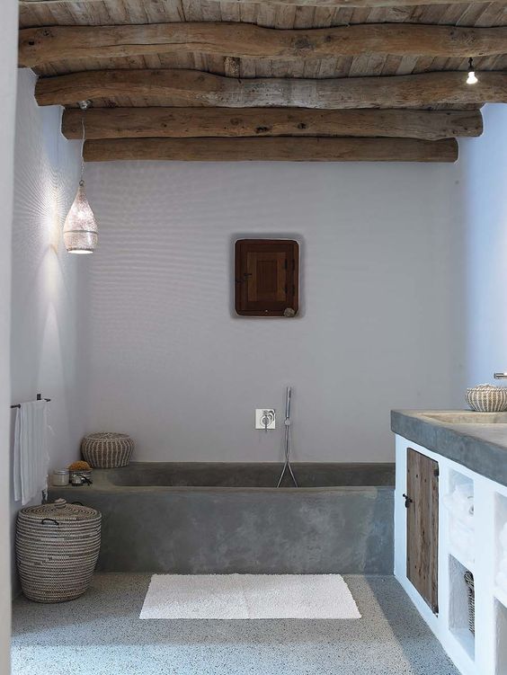 a chic bathroom with white walls, a concrete bathtub, a wooden ceiling and beams and a concrete vanity